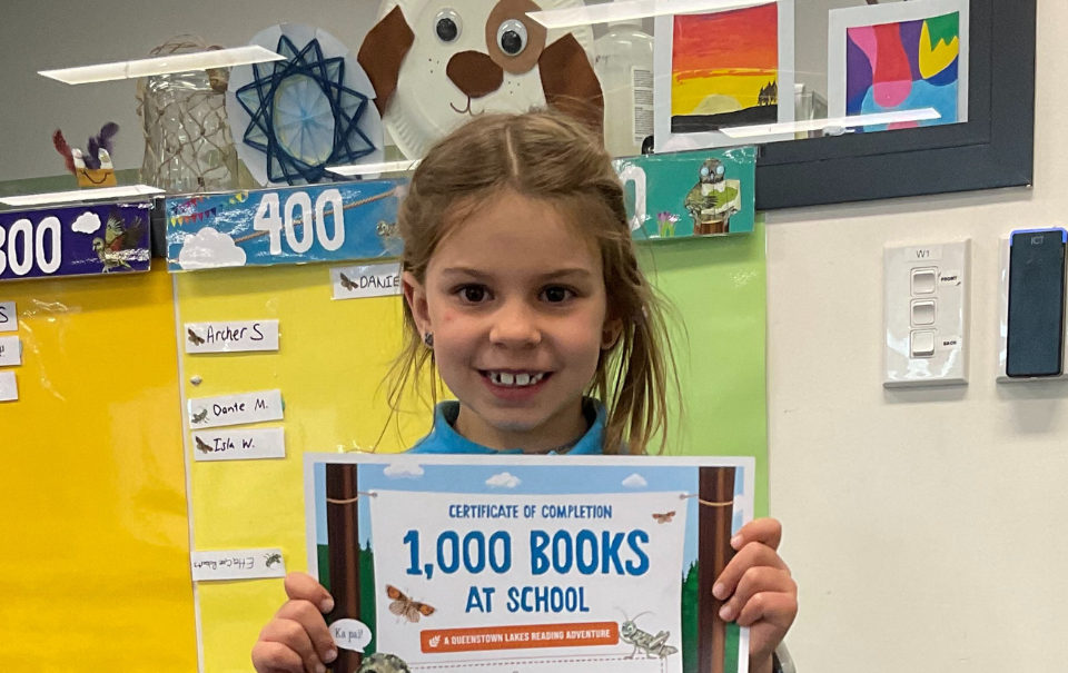 Sophia, our first 1,000 Books at School graduate posing in the library with her completion certificate